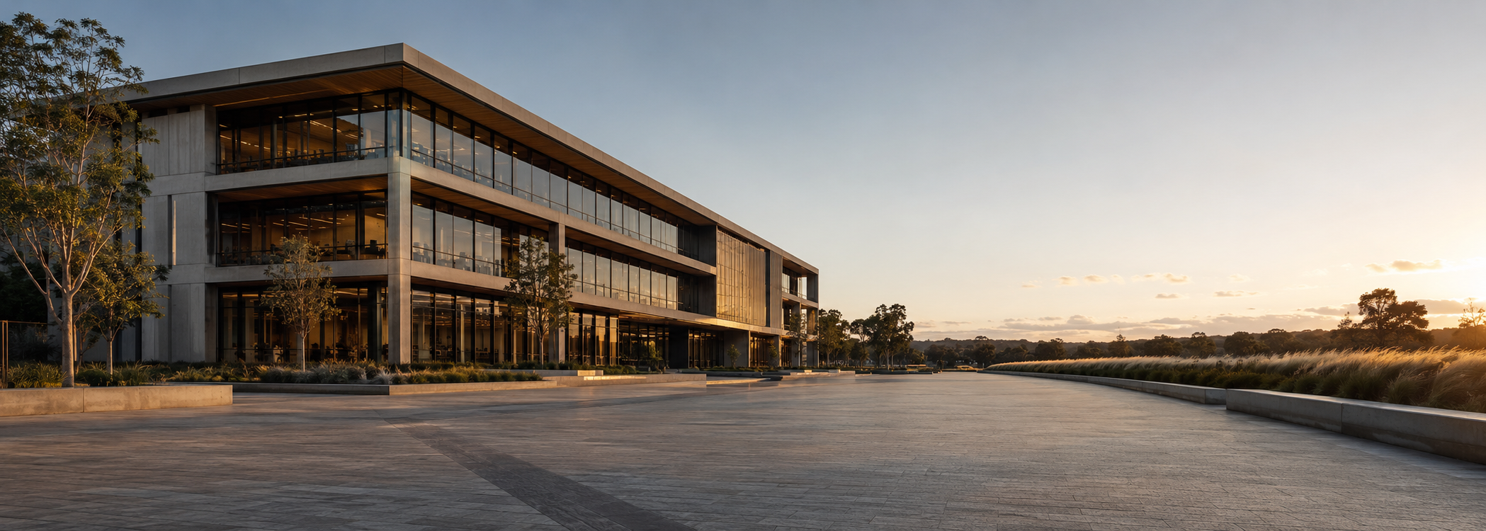 Modern Australian commercial building with warm concrete, deep glazing and a calm paved forecourt in late afternoon light.